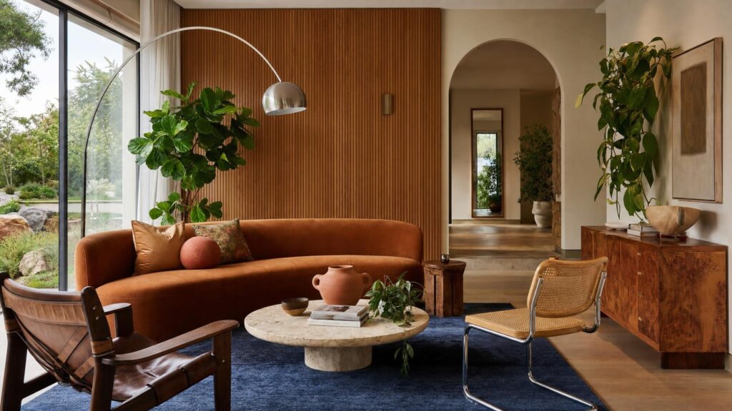 Living room styled with 2026 interior trends, with a curved rust velvet sofa, fluted timber wall, arched doorway and indigo rug